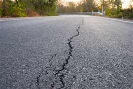 Close-up of a new asphalt road surface with a crack running through it to represent construction corruption.