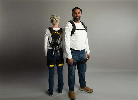 A woman with her back facing the camera and a man facing the camera, both wearing the HeroWear Apex 2 exoskeleton